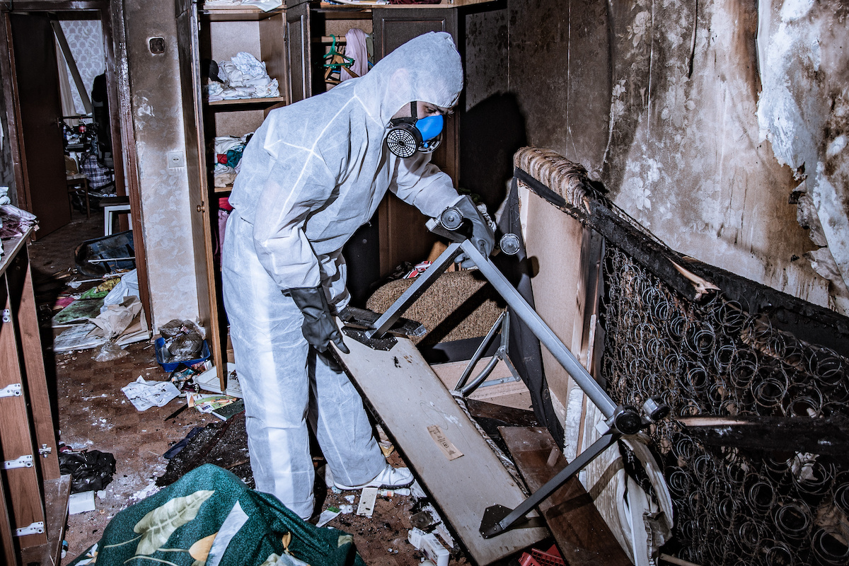 A specialist in a protective suit from a fire restoration company cleans a destroyed housing after a fire.