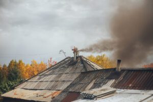 The Effects of Smoke Damage on Your Home and Health - Valley Restoration Chimney sweep cleaning a chimney standing balanced on the apex of a house roof lowering equipment down the flue